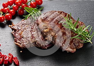 Two fried ribeye beef pieces on a black slate board, rare degree of doneness. Appetizing steak