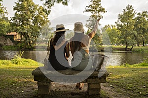 two friend girls with hats chatting sitting on a stone bench in front of the river