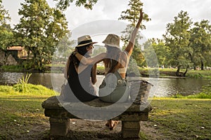 two friend girls with hats chatting sitting on a stone bench in front of the river