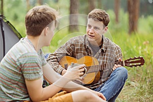 Two friend sitting in the tent, play the guitar and sing songs