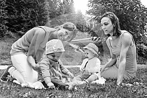 Two friend women enjoying a picnic in a beautiful sunny day with their little daughters - Women sitting with little baby girls on
