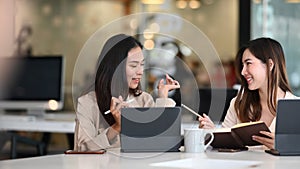 Two friendly businesswomen are discussing new ideas while working on computer tablet.