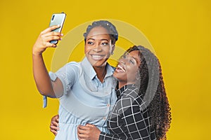 Two friends african american girls take a selfie or video call with friends on a yellow background. video chat, video conference