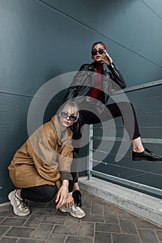 Two friends beautiful young women in fashionable clothes with leather twist and jeans posing on the street