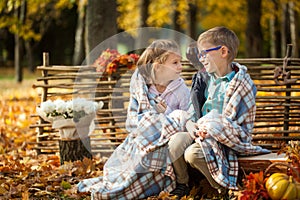 Two friends: a boy and a girl in autumn park sitting on wooden bench near a fence