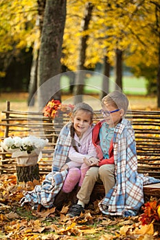 Two friends: a boy and a girl in autumn park sitting on wooden bench near a fence