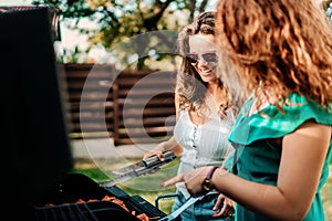 Two female friends cooking on barbeque grill, having lunch in nature with friends