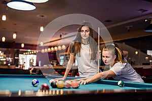 Two friends with cues in pub. They wearing casual wear and playing billiard