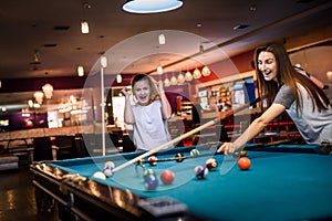 Two friends with cues in pub. They wearing casual wear and playing billiard