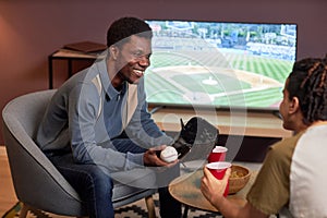Two friends discussing baseball match at home and smiling cheerfully