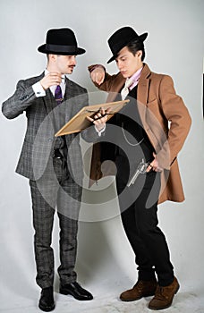 Two friends dressed in vintage clothes and depict retro detectives and spies in English classic style on a white studio background