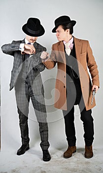 Two friends dressed in vintage clothes and depict retro detectives and spies in English classic style on a white studio background