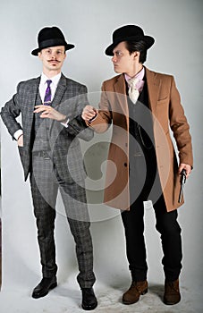 Two friends dressed in vintage clothes and depict retro detectives and spies in English classic style on a white studio background