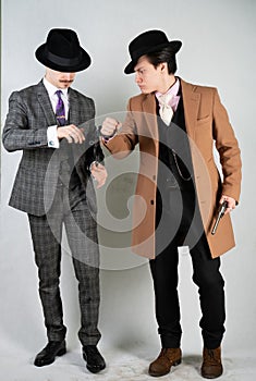 Two friends dressed in vintage clothes and depict retro detectives and spies in English classic style on a white studio background