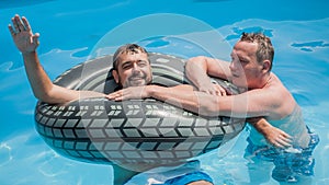 Two friends floating on swimming pool with inflatable rings