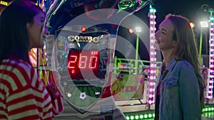 Two friends hang out at funfair machine. Smiling girls playing in amusement park