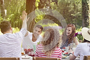 Two friends high-fiving each other and their girlfriends laughing during a garden party in the summer