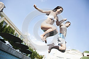 Two friends holding hands and jumping into a pool, mid-air