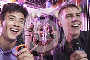 Two friends holding microphones and singing together at karaoke, friends in the background