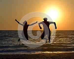 Two friends jumping on beach during sunrise