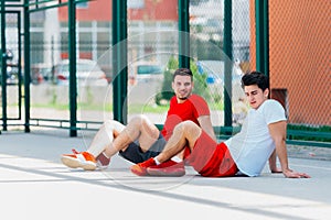 Two friends after a long hard basketball game have some rest on the basketball court sitting next to each other and have a