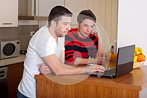 Two friends men using laptop in kitchen
