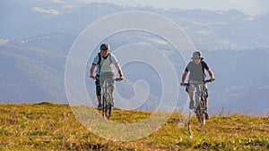 Two friends pedalling their mountain bikes up a hill during a cycling adventure.