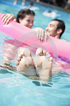 Two friends in a pool holding onto an inflatable raft with feet sticking out of the water