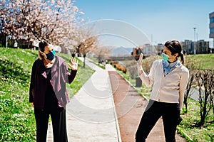 Two friends with protective masks greet with waving to each other.Alternative greeting during quarantine to avoid physical contact photo