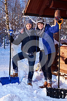 Two friends shoveling snow from the yard in winter cottage