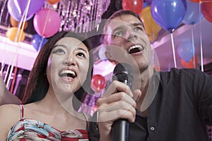 Two friends singing into a microphone together in a nightclub for karaoke