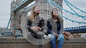 Two friends sit on a wall at Tower Bridge London