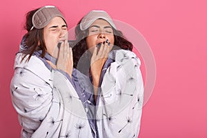 Two friends standing together over pink background, yawning and covering mouth with hands, restless and sleepiness, dark haired photo