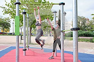 Two friends swinging in a monkey bar at a calisthenics park wearing protective face masks