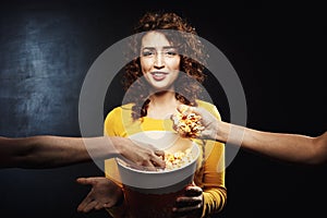 Two friends taking popcorn from girl`s bucket. Negative facial emotions