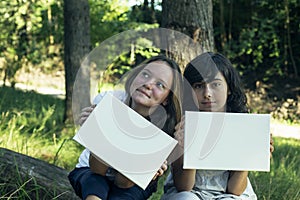 Two friends teengirl holding clean white sheet paper banner for your message in the park.