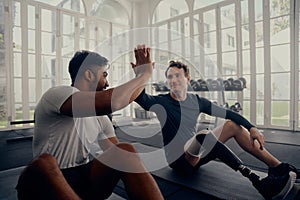 Two friends training in the gym - one with a prosthesis . Two men high fiving in the gym after a good training session