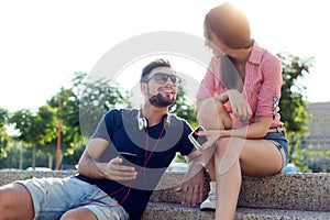 Two friends using mobile phone and listening to music in the str