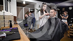 Two friends visiting modern barbershop. Handsome hipsters sitting against mirror and working with hairstylists. Smiling