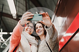 Two friends waiting going down stairs at the station before catching a train. Taking selfie with mobile phone. Travel photography