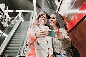 Two friends waiting going down stairs at the station before catching a train. Taking selfie with mobile phone. Travel photography