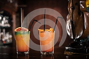 Two fruit alcoholic cocktail with straw at the bar table