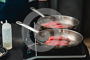 Two frying pans with tuna steak on induction stove