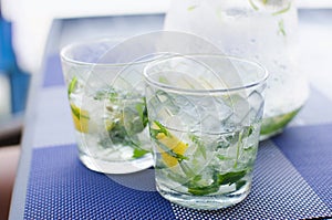 Two full glasses of fresh cool transparent water with ice, lemon and , basil leaves