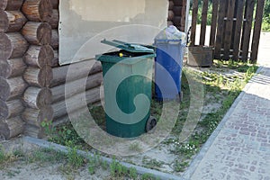 Two full plastic trash cans stand on green grass and ground outside