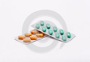 Two full sealed packages - one with orange rectangular pills and one with rectangular shaped green pills lie on white background