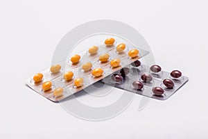 Two full sealed packages - one with yellow oval shaped pills and one with brown oval shaped pills lie on a white background