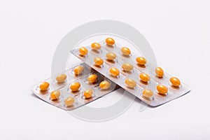 Two full sealed packages with yellow oval shaped pills lie on a white background