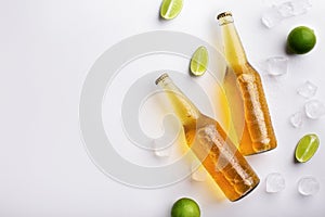 Two full transparent glass bottles with ale without labels, with flowing drops, lie with ice and pieces of lime