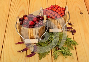 Two full wooden bucket with rose hips and Rowan on table